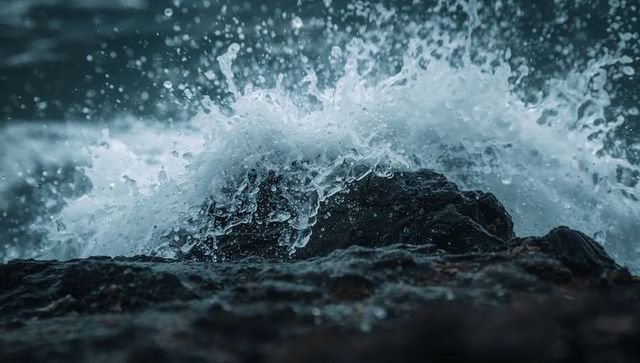 Crashing ocean wave hitting dark jagged rock, spray and foam exploding over shoreline