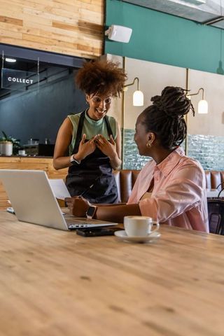 African american barista chatting with customer at coworking cafe with laptop and coffee