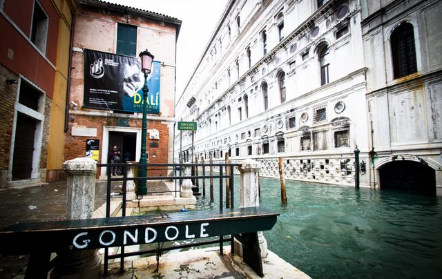 This image captures a flooded canal in Venice, Italy, with historical buildings and a 'Gondole' sign prominently displayed. The floodwaters create an intriguing reflection of the architecture against the backdrop. Ideal for tourism ads, travel blogs, historical architecture studies, urban flooding reports, and cultural exploration articles.