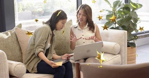 Two women collaborating on laptop and tablet in bright lounge with gold star overlays, coworking