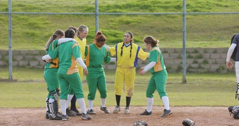 Female softball team huddling in green and yellow uniforms