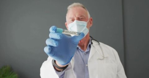 Senior physician holding vaccine vial wearing mask and blue gloves with stethoscope