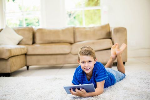 Happy Boy Relaxing With Tablet on Cozy Living Room Carpet