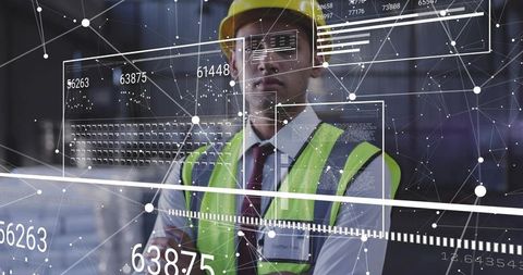 Engineer examining digital analytics overlay in warehouse wearing hard hat hi-vis vest