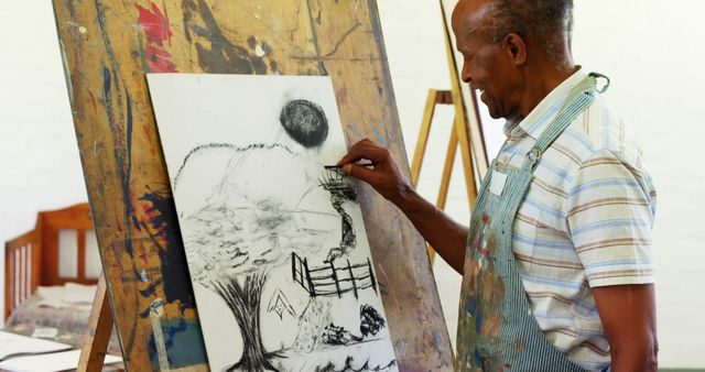 An African American senior man focuses on creating a charcoal drawing on an easel, with copy space. His artistic expression and concentration are evident as he works on detailing his artwork.