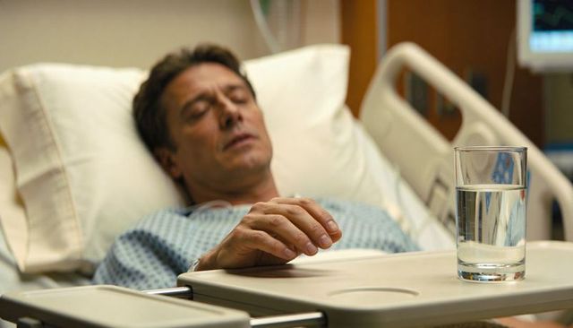 Middle-aged man resting in hospital bed with hand on overbed tray and glass of water