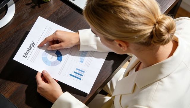Pointing businesswoman reviewing strategy report with pie and bar charts at modern desk