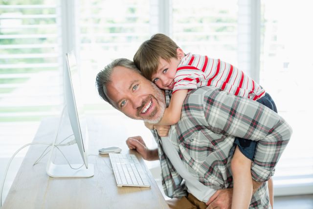 Father and son enjoying time together while using a computer at home. Ideal for themes related to family bonding, parenting, home office, and technology use in everyday life.