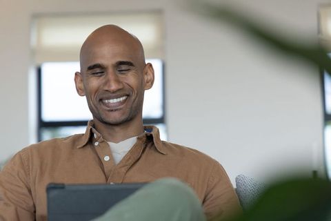 Middle-aged african american man smiling while using tablet on couch in sunlit lounge