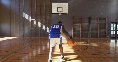 Dribbling player in no.10 jersey heading to hoop on sunlit hardwood basketball court