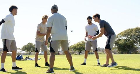 Young men playing catch and team drills on sunlit park lawn building teamwork and fitness