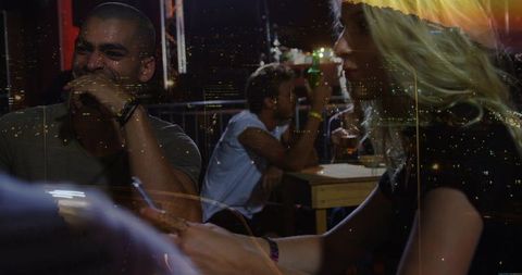 Laughing man and blonde woman sharing phone at urban bar with city lights and reflections