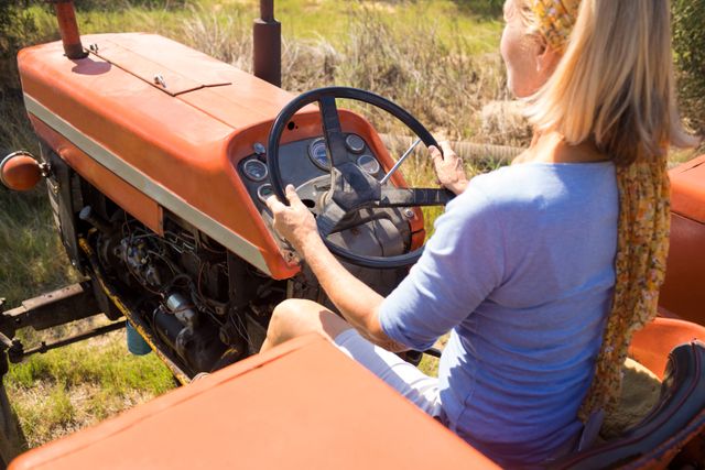 This image depicts a woman driving a tractor in an olive farm on a sunny day. Ideal for use in agricultural promotions, rural lifestyle blogs, farming equipment advertisements, and articles about women in agriculture.