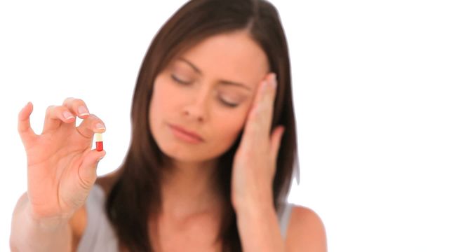 A woman experiencing a headache holds a pill in hand while touching her forehead. This conveys themes of health issues, relief from pain, and medical solutions. Useful for health-related articles, advertisements for medication, or illustrating personal healthcare choices.