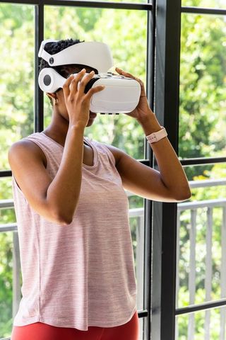 African woman using vr headset for home fitness workout on balcony wearing pink watch