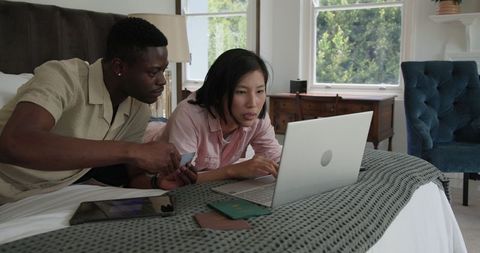 Diverse Couple Collaborating on Technology in Bedroom