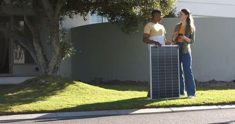 Diverse couple inspecting solar panel on lawn while using phone for home solar planning