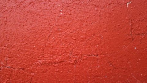 Cracked red stucco wall revealing lighter substrate, textured paint peeling and fissures