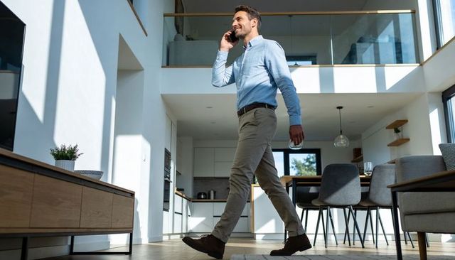 Man walking and talking on phone in sunlit open-plan modern home interior