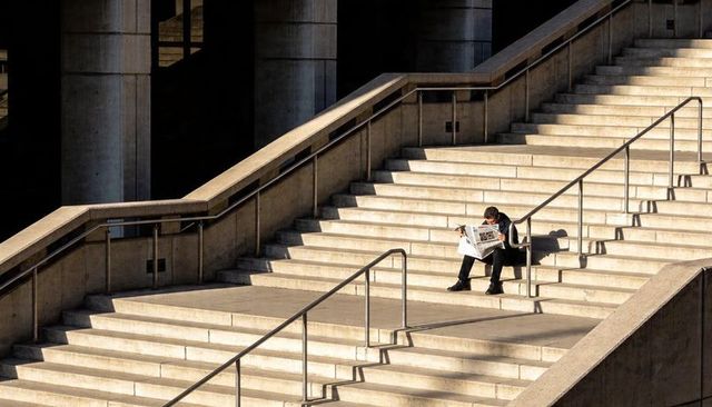 Businessman Reading Newspaper on Wide Concrete Stairs in Sunlit Urban Plaza, Strong Lines