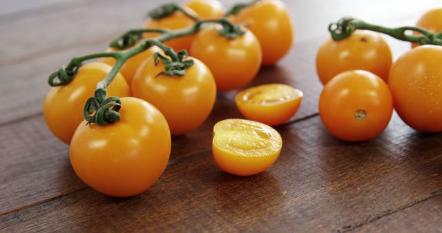 Fresh yellow cherry tomatoes are resting on a rustic wooden table with a few cut open to show their juicy interior. Perfect for promoting healthy eating, organic produce, seasonal recipes, and farmhouse kitchen settings.