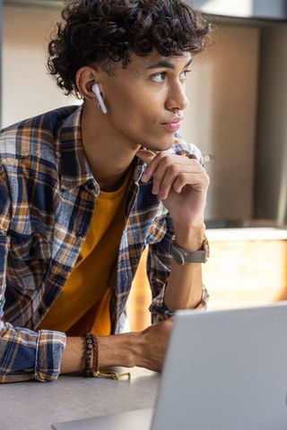 Young Man Reflecting in Kitchen with Laptop and Earbuds