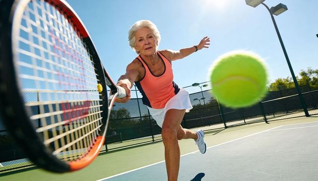Senior woman lunging to return tennis ball on outdoor court, dynamic active lifestyle