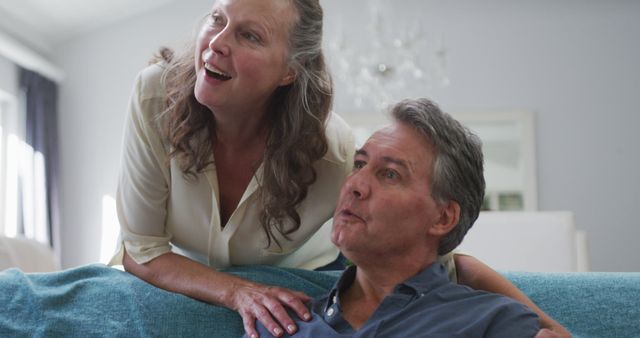 Happy senior caucasian couple watching tv in living room and talking, wife embracing sitting husband. retirement lifestyle together at home.
