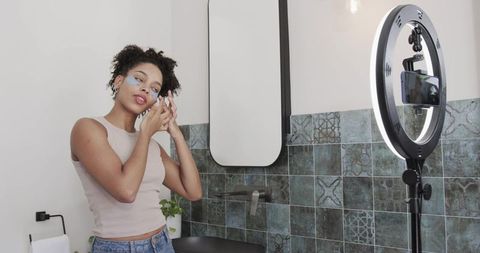 Filming skincare routine: applying under-eye patches with ring light and smartphone