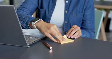 Peeling sticky note while working on laptop at minimalist home office desk
