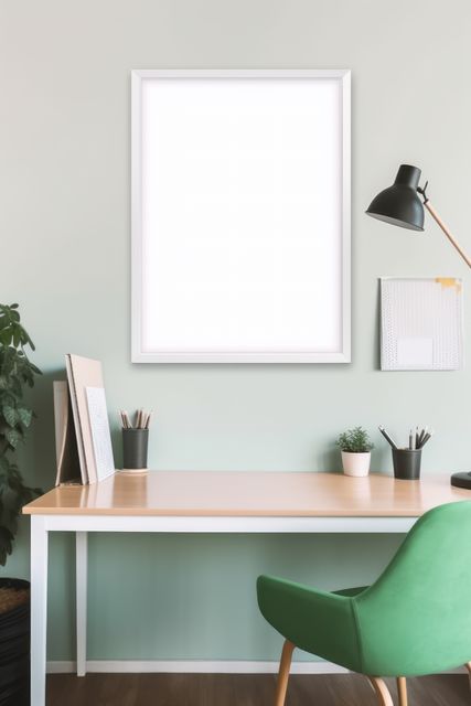 Modern home office featuring blank white frame on sage green wall over light wood desk with green chair. Perfect for showcasing interior design ideas, workspace organization tips, or promoting productivity tools.