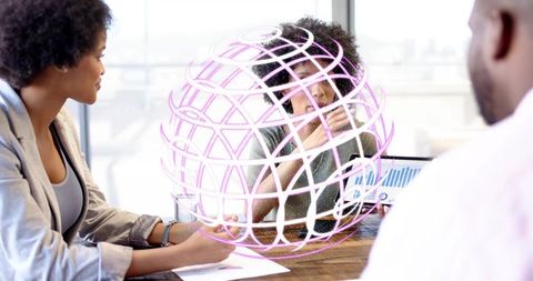 Team collaborating around holographic globe with data analytics on laptop in modern office