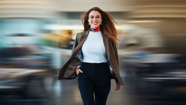 Confident businesswoman walking through modern office with motion blur wearing colorful scarf and gl