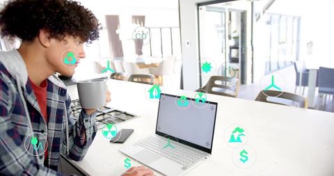 Young man checking laptop while sipping coffee in modern kitchen with sustainability icons