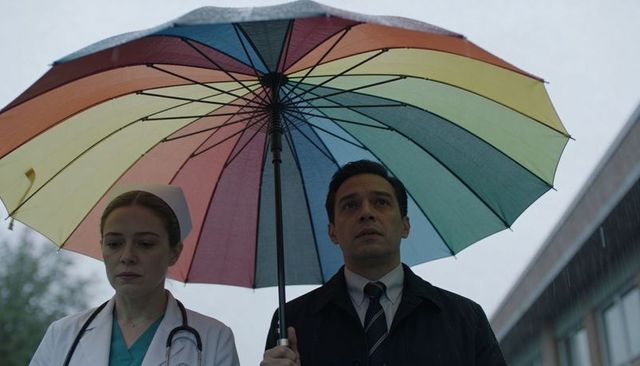 Medical professionals standing under rainbow umbrella in rain outside hospital