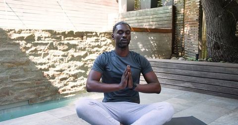 Man Meditating Outdoors on Patio Near Pool