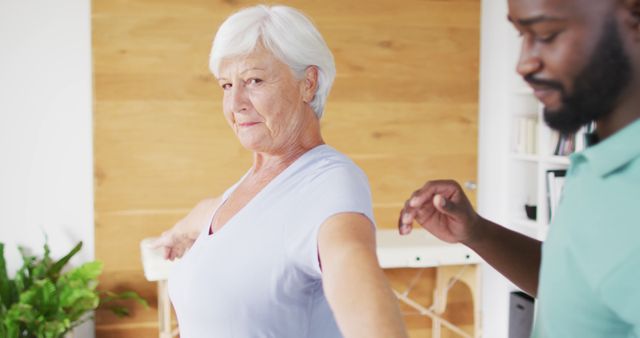 Elderly white woman receiving physical therapy at home assisted by a caregiver. Used for themes on senior care, rehabilitation exercises, home healthcare services, and maintaining wellness in aging.