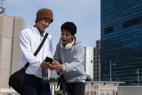 Diverse teen friends sharing smartphone on urban rooftop with city skyline