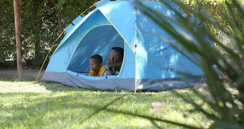 African american father and son relaxing in backyard tent watching sunlight and nature