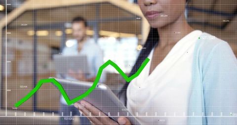Businesswoman holding tablet analyzing green upward trend graph overlay with coworker in office