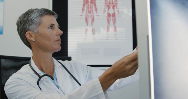 Mature female doctor studies x-ray image in medical office. Ideal for healthcare, medical research, doctor profiles, radiology articles, and hospital promotions.