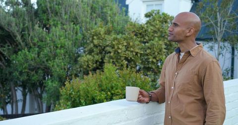 Indian man standing on balcony holding mug enjoying morning garden view