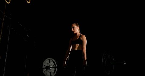 Female athlete lifting barbell in dark gym
