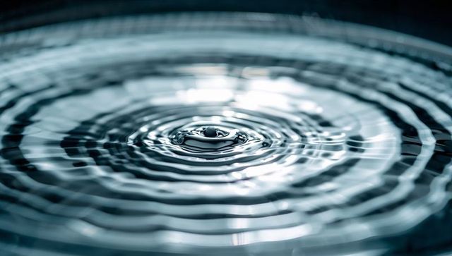 Forming water droplet crown with concentric ripples and reflective gleam minimal blue macro