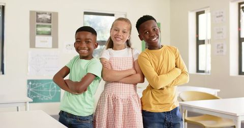 Confident diverse students standing with arms crossed and smiling in bright classroom