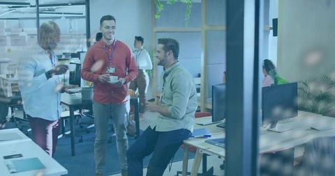 Coworkers chatting over coffee in modern open-plan office with greenery