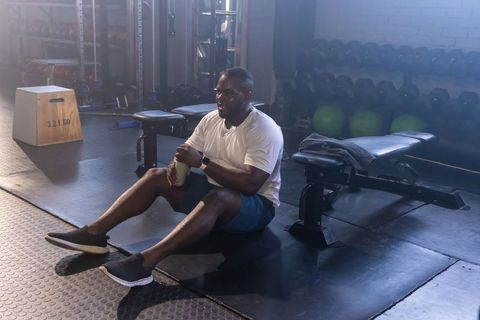 Athlete sitting on gym floor holding water bottle after strength training, resting