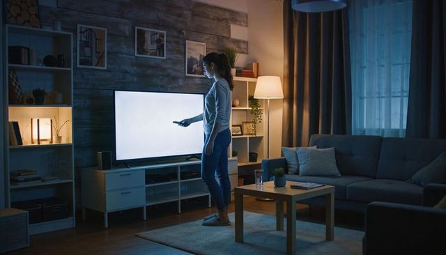 Woman pointing remote at tv in cozy modern living room, evening ambient lighting