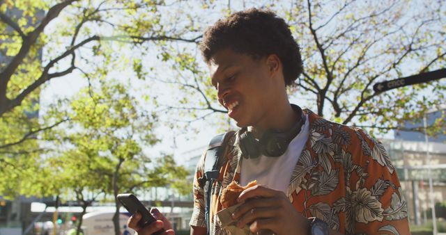 Young Man Enjoying Urban Park with Smartphone and Snack on Sunny Day - Download Free Stock Images Pikwizard.com