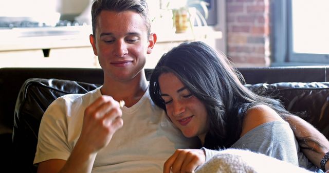 Young couple enjoying leisure time, sitting on sofa, smiling and showing affection towards each other. Perfect for articles, blog posts on relationships, lifestyle, happy moments at home, or advertising comfortable living spaces.
